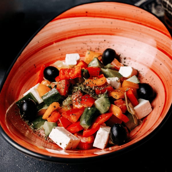 Colorful Greek salad with red and orange bell peppers, cucumbers, black olives, and feta cheese.