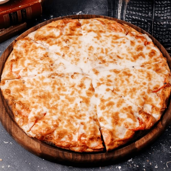 A round, cheesy Valley Pizza, sliced into wedges, on a wooden serving board.