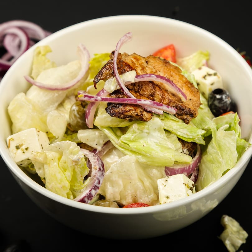 A white bowl of Valley Pizza's salad with grilled chicken, lettuce, red onion, feta, and olives.