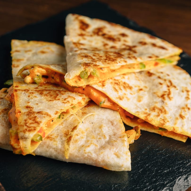 Golden-brown quesadilla triangles with melted cheese and green peppers on a dark plate.